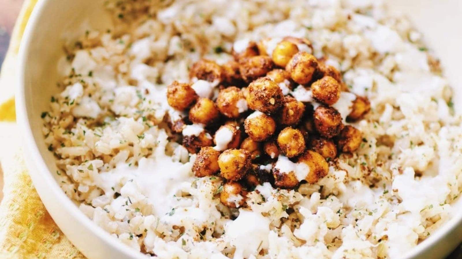 A bowl of rice topped with seasoned chickpeas, herbs, and a drizzle of creamy white sauce.