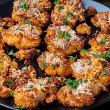A plate of roasted cauliflower steaks garnished with herbs and grated cheese.