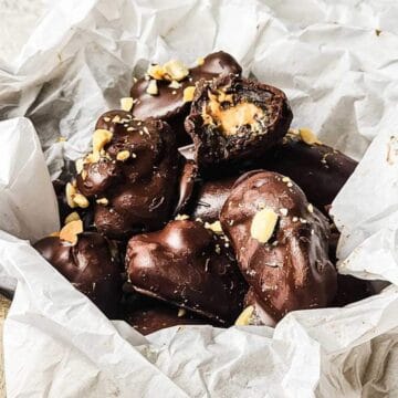 Chocolate-covered candies with a peanut butter filling, topped with crushed nuts, in a box lined with parchment paper.
