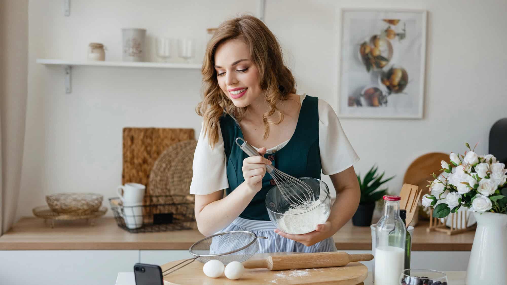 Woman whisking flour in a bowl in a kitchen, with eggs and baking ingredients on the counter—perfect for those who appreciate Gifts That Make Holiday Cleanup Easier.