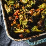 Duck Fat Roasted Vegetables, including broccoli, chickpeas, and potatoes, in a blue baking dish on a gray surface.