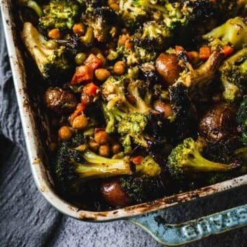 Duck Fat Roasted Vegetables, including broccoli, chickpeas, and potatoes, in a blue baking dish on a gray surface.