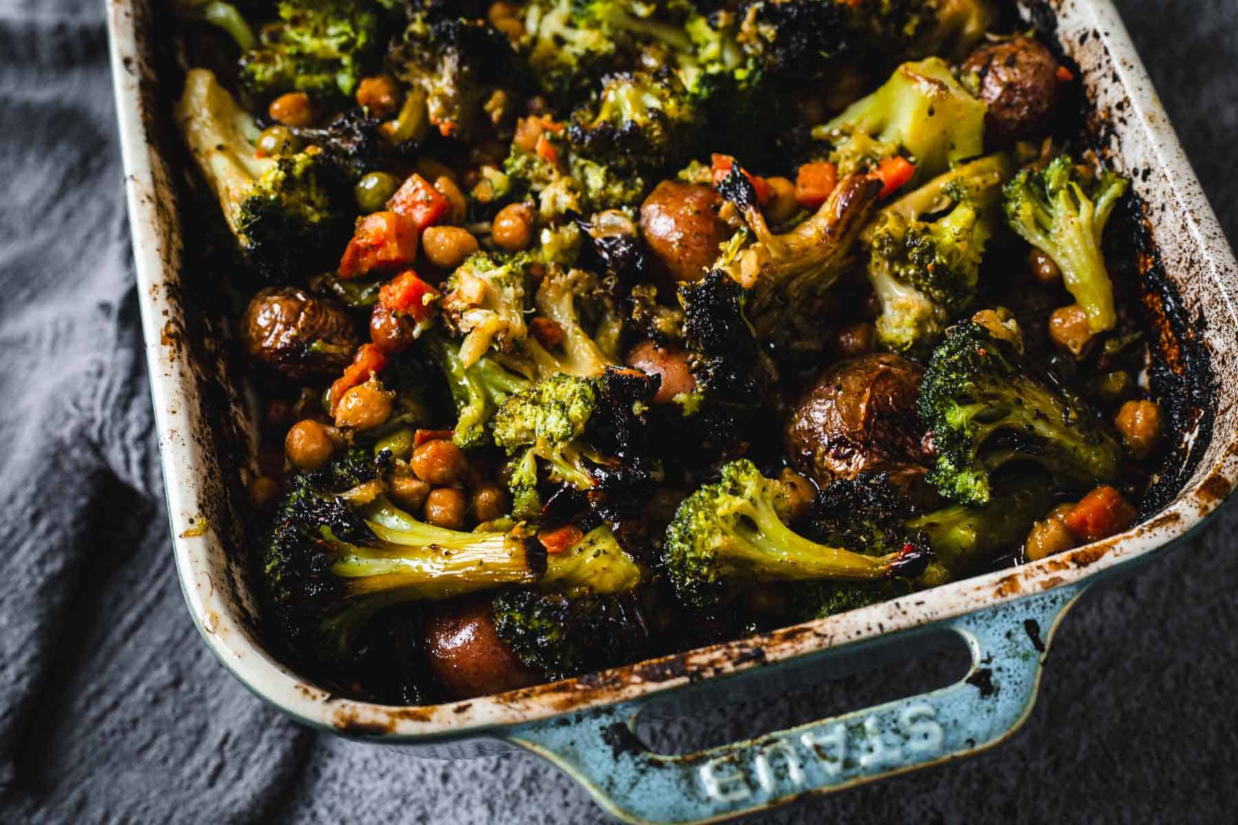 Duck Fat Roasted Vegetables including broccoli, carrots, potatoes, and chickpeas are arranged in a ceramic baking dish for a rich, savory flavor.