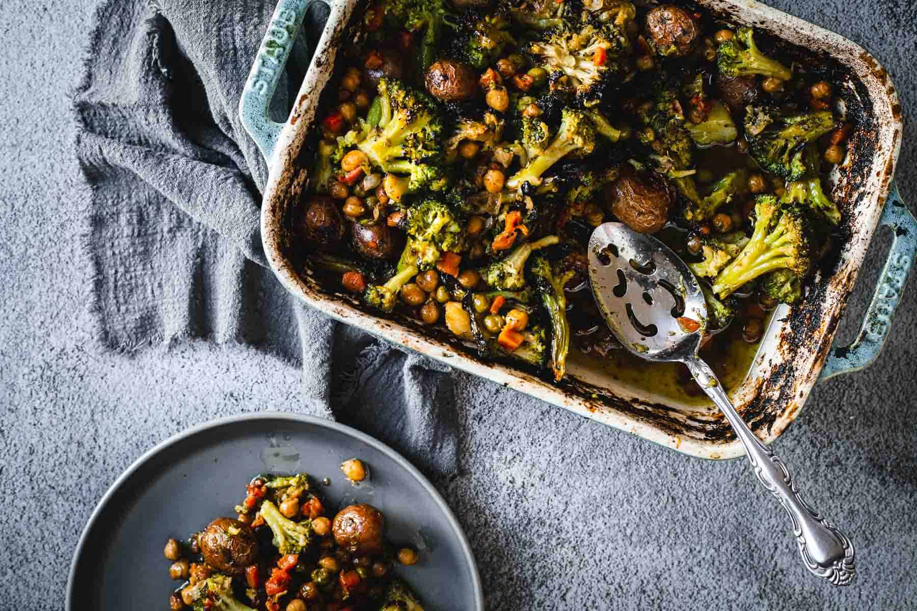 A baking dish with Duck Fat Roasted Vegetables&mdash;broccoli, mushrooms, and chickpeas&mdash;next to a plate of the same savory vegetables.