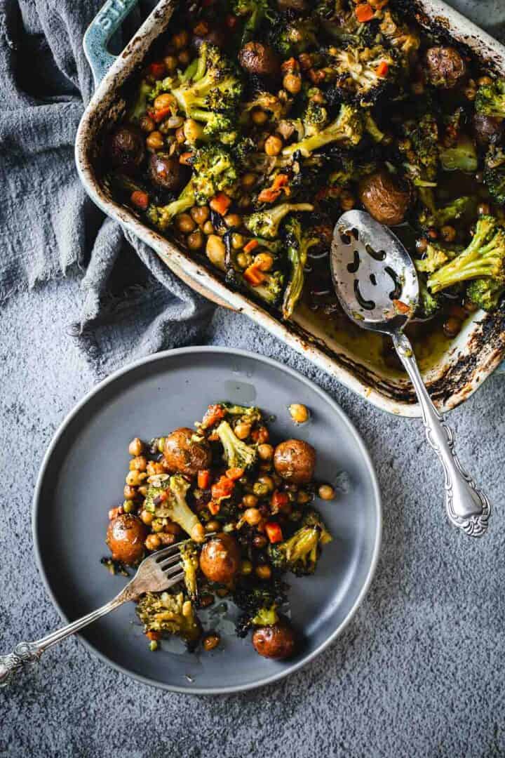 Duck Fat Roasted Vegetables with chickpeas served on a gray plate, beside a baking dish with more of the same.