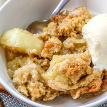 A bowl of apple crumble with a scoop of vanilla ice cream and cinnamon sticks beside it.
