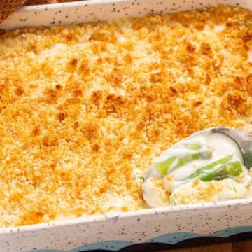 Casserole dish with a golden breadcrumb topping, a serving spoon reveals creamy filling with green beans.