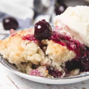 A bowl of cherry cobbler topped with vanilla ice cream and whole cherries.