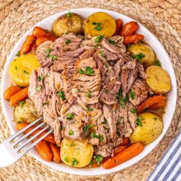 A bowl of shredded pot roast with baby potatoes and carrots, garnished with parsley, on a woven placemat.