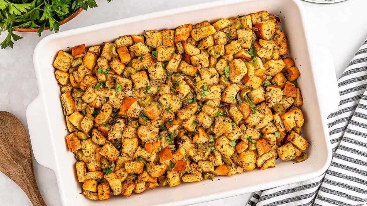 A casserole dish filled with golden, cubed bread stuffing garnished with herbs.