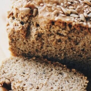 A loaf of seeded whole grain bread on a wooden surface with one slice cut.