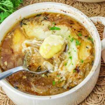 A bowl of French onion soup topped with melted cheese and herbs, with a spoon inside the bowl.