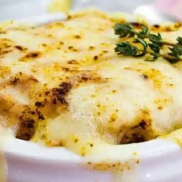 A bowl of baked lasagna topped with melted cheese and garnished with fresh herbs.