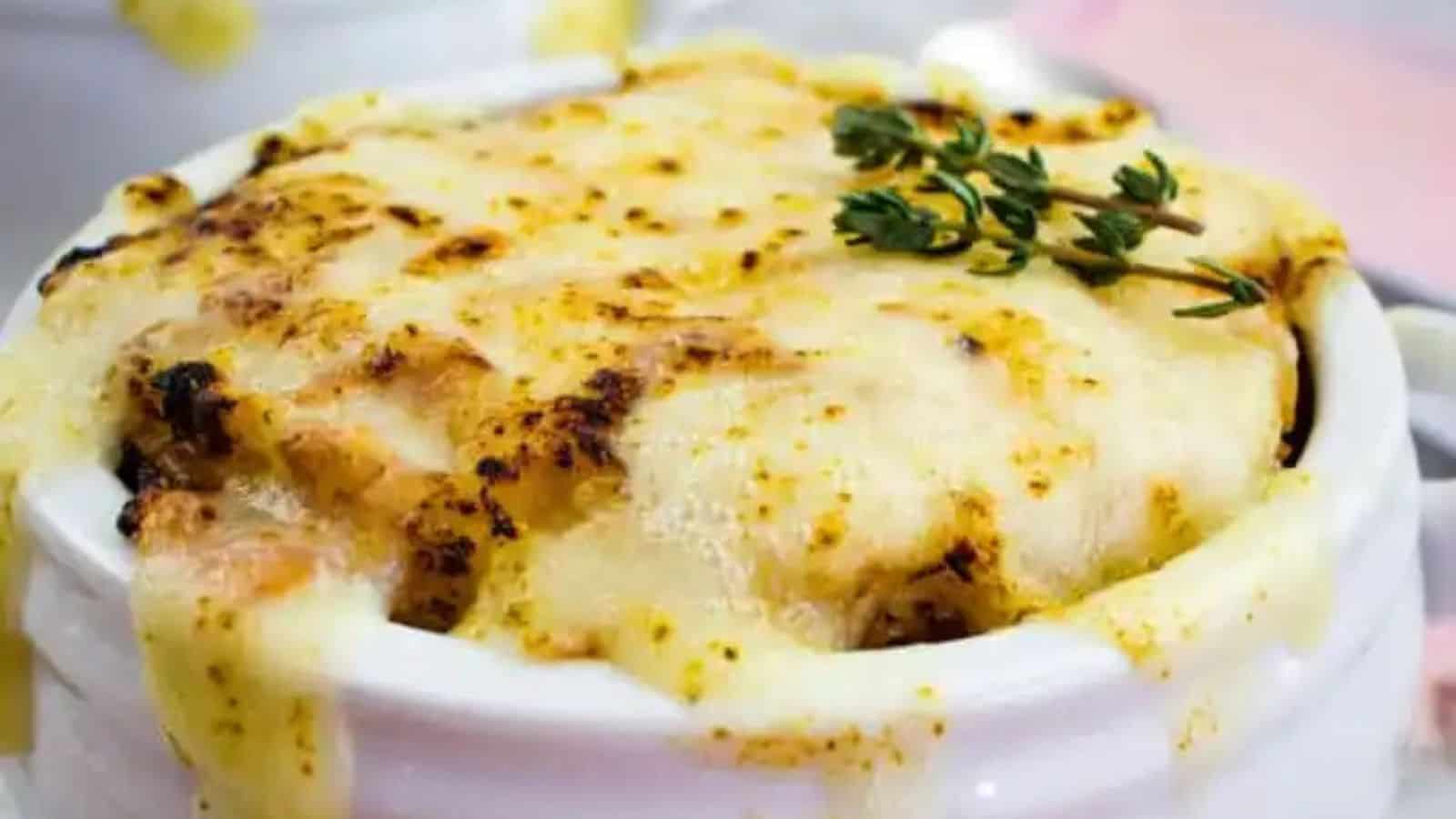 A bowl of baked lasagna topped with melted cheese and garnished with fresh herbs.