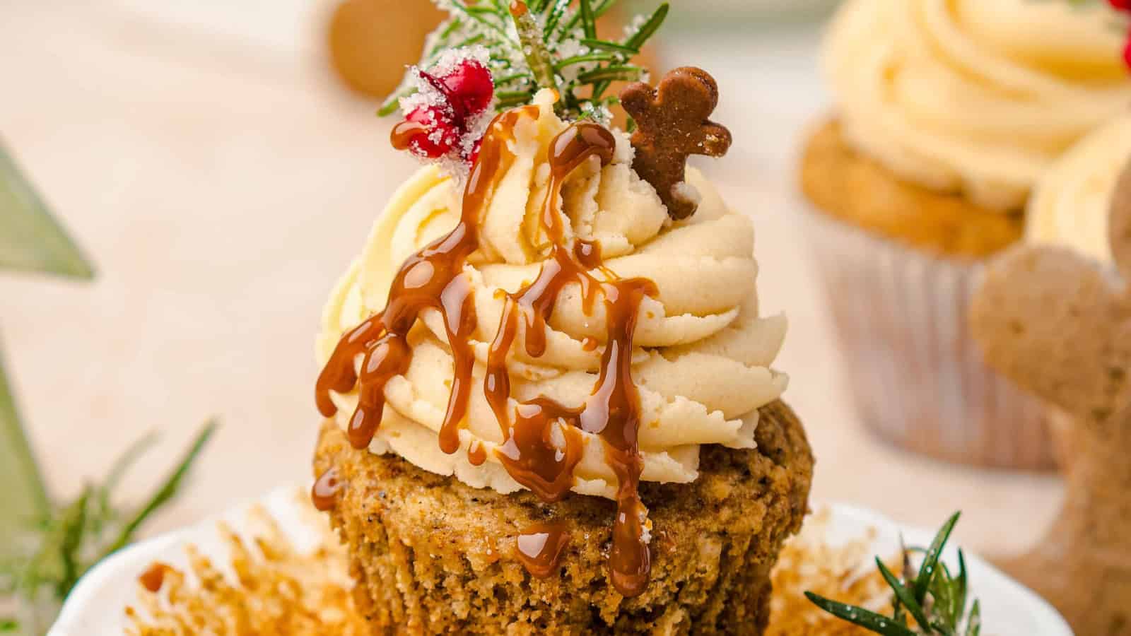 Cupcakes with cream frosting, rosemary, berries, and gingerbread cookies on white plates, festive background.