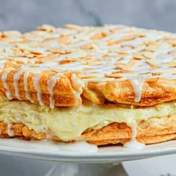 A layered almond pastry cake with cream filling, drizzled with white icing and topped with sliced almonds.