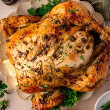 Roast chicken garnished with herbs on a plate, surrounded by lemon wedges, parsley, and green beans.