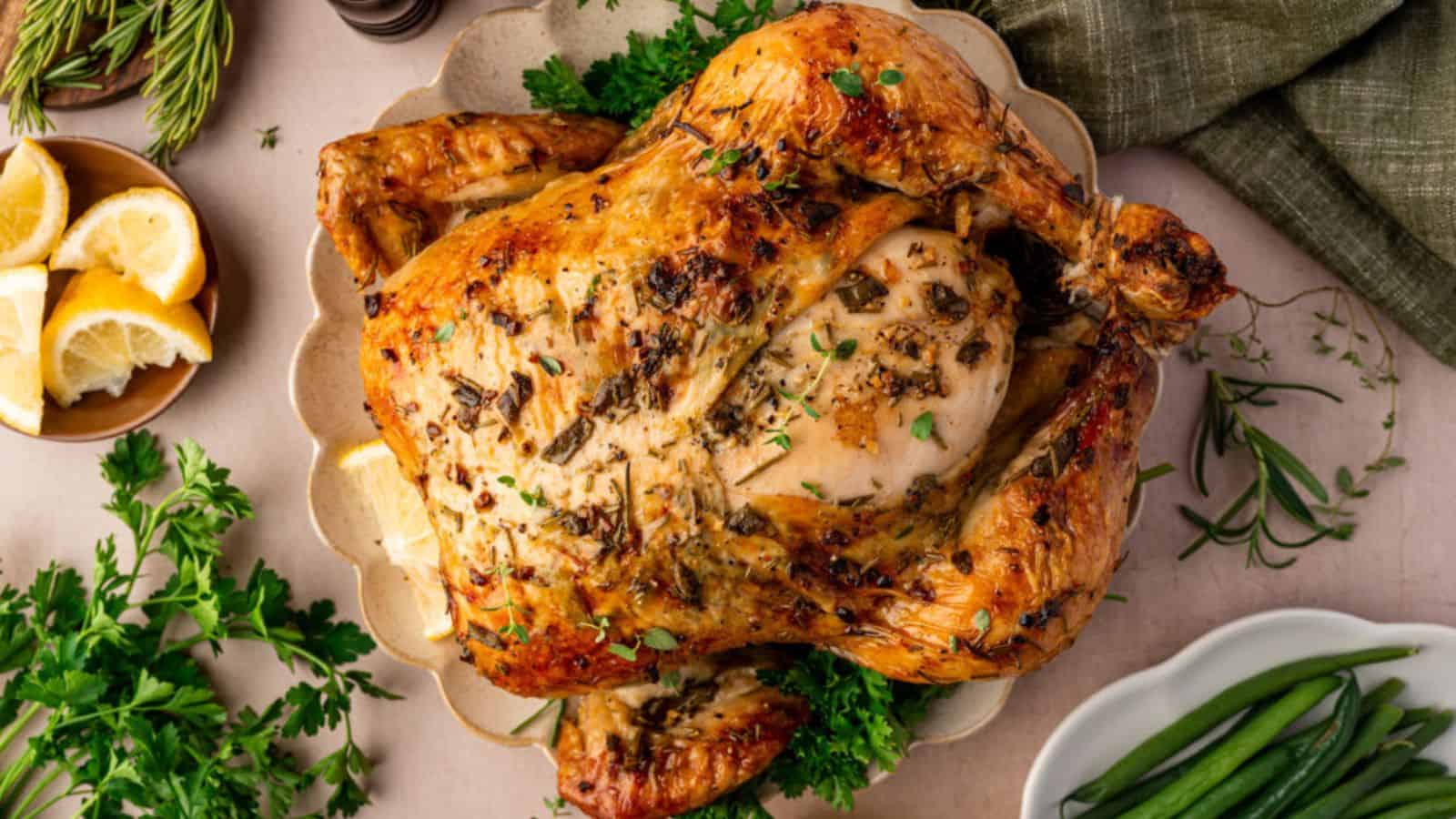 Roast chicken garnished with herbs on a plate, surrounded by lemon wedges, parsley, and green beans.