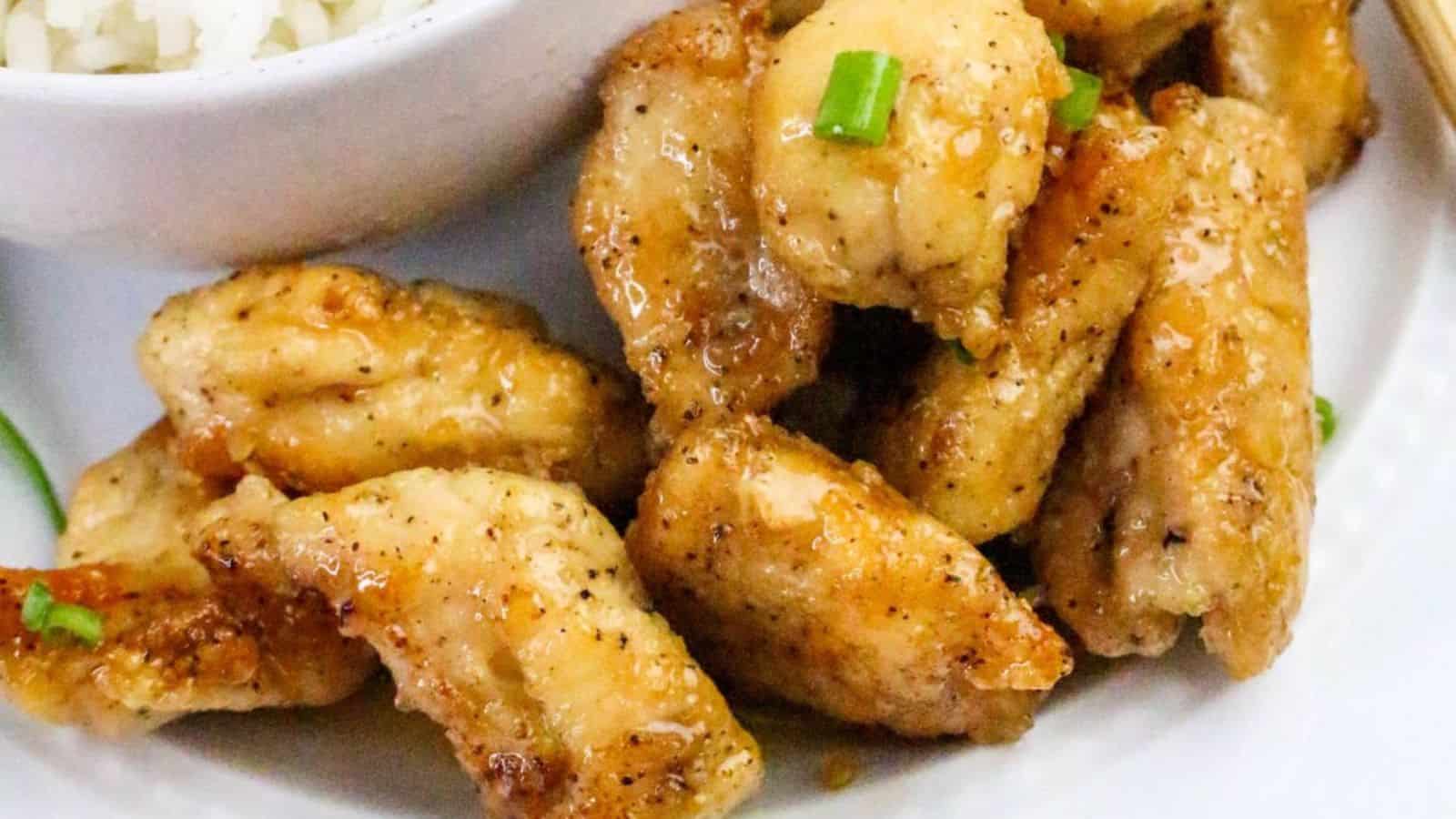 Golden brown pieces of seasoned chicken garnished with green onion, served next to a bowl of white rice.