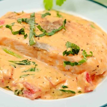 Salmon fillet topped with creamy sauce, spinach, and herbs, served on a white plate with a blue rim.