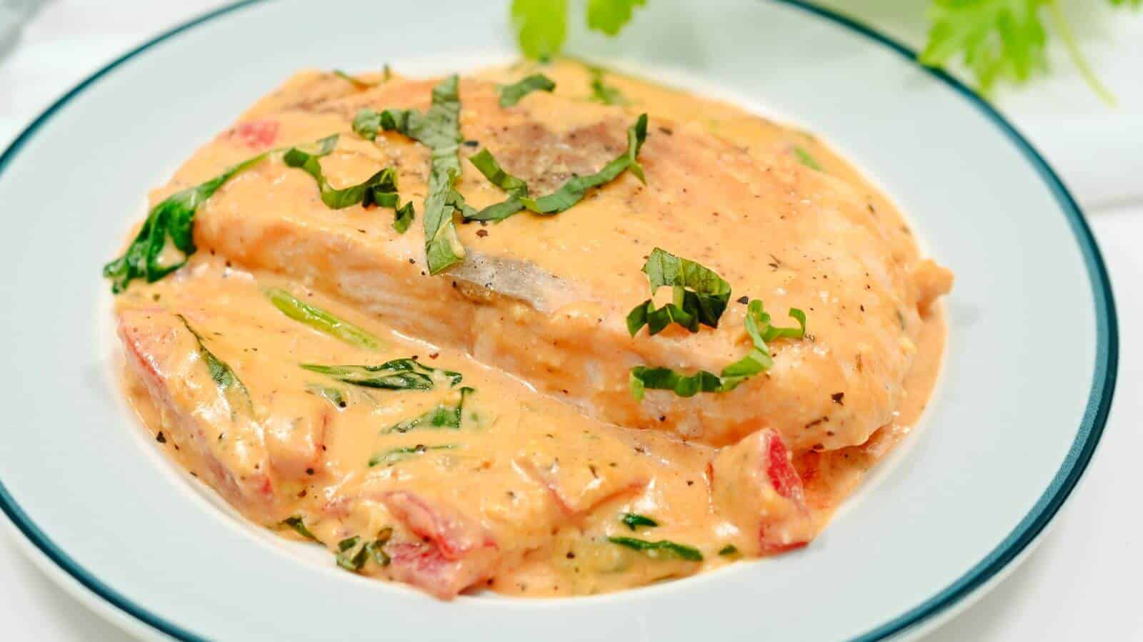 Plate of salmon in creamy sauce garnished with chopped herbs, featuring spinach and red peppers.