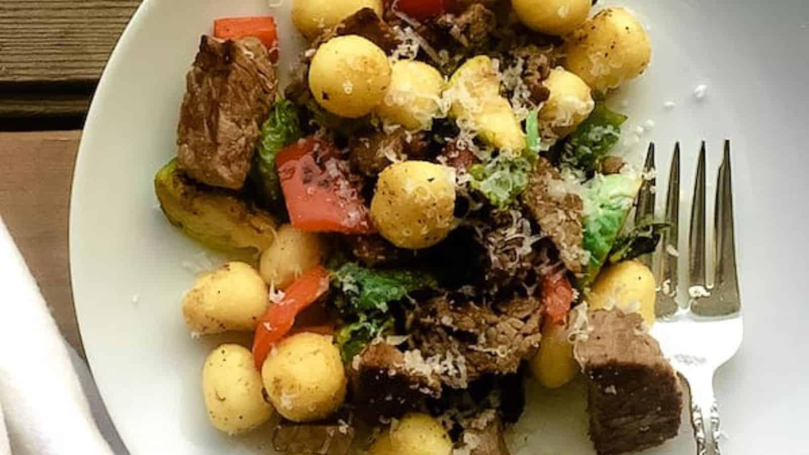 Leftover prime rib, gnocchi, and vegetables on a plate.