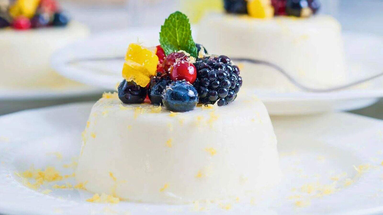 A panna cotta dessert topped with fresh berries, mint, and lemon zest on a white plate.