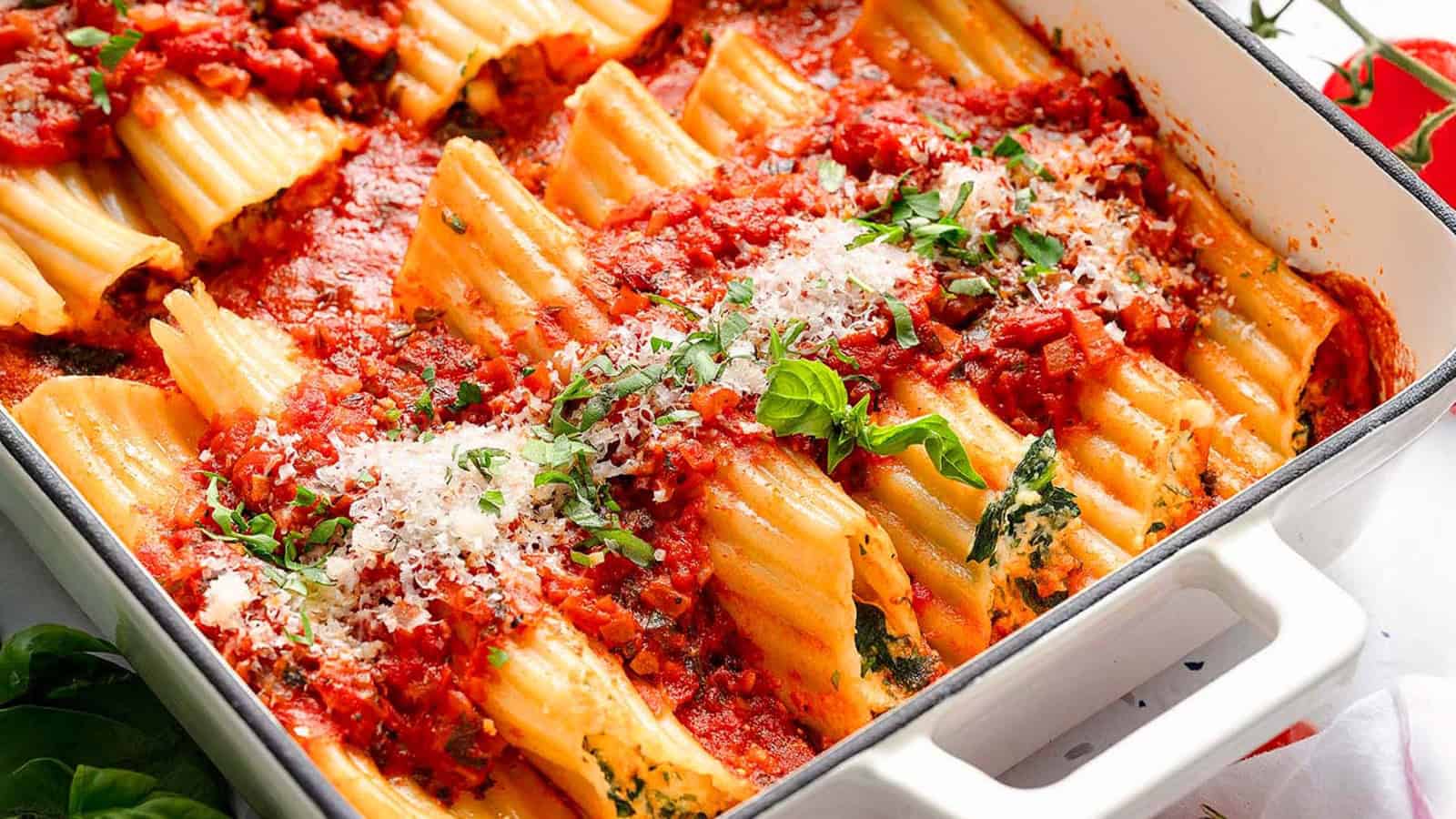 Baked manicotti pasta filled with spinach and ricotta, topped with tomato sauce, herbs, and grated cheese in a white dish.