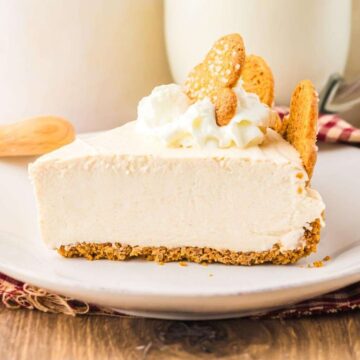 A slice of creamy cheesecake with whipped cream and cookies on top, served on a white plate.