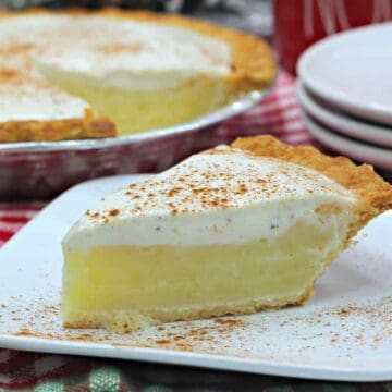 A slice of creamy custard pie with whipped topping and cinnamon sits on a plate, with the whole pie in the background.
