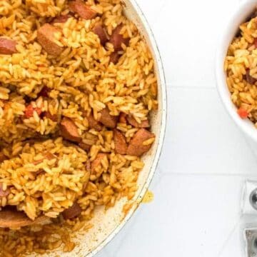 A pot and bowl of seasoned rice with sausage pieces, with a wooden spoon and salt and pepper shakers nearby.