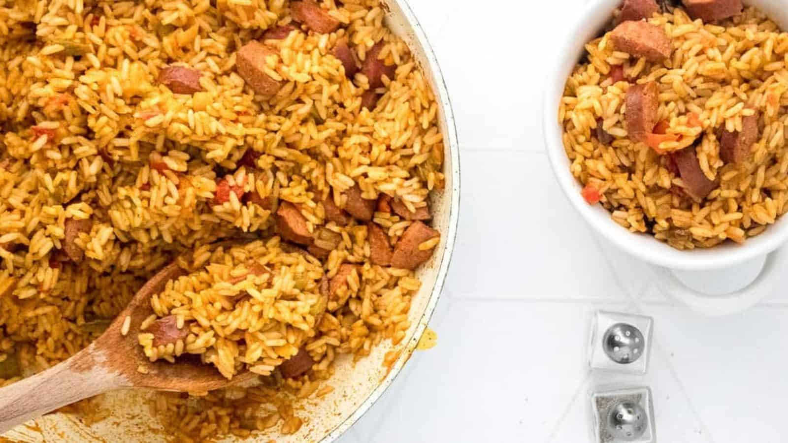 A pot and bowl of seasoned rice with sausage pieces, with a wooden spoon and salt and pepper shakers nearby.