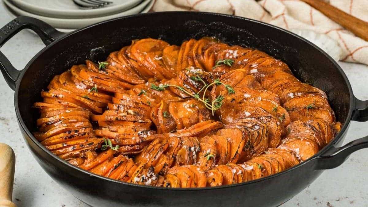 Sliced roasted sweet potatoes arranged in a cast-iron skillet, garnished with fresh herbs and sea salt.