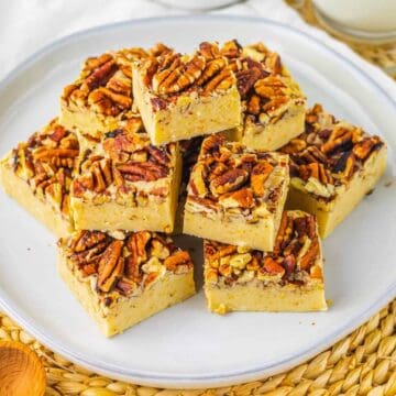 A plate of pecan-topped dessert bars stacked on a white plate, set on a woven placemat.