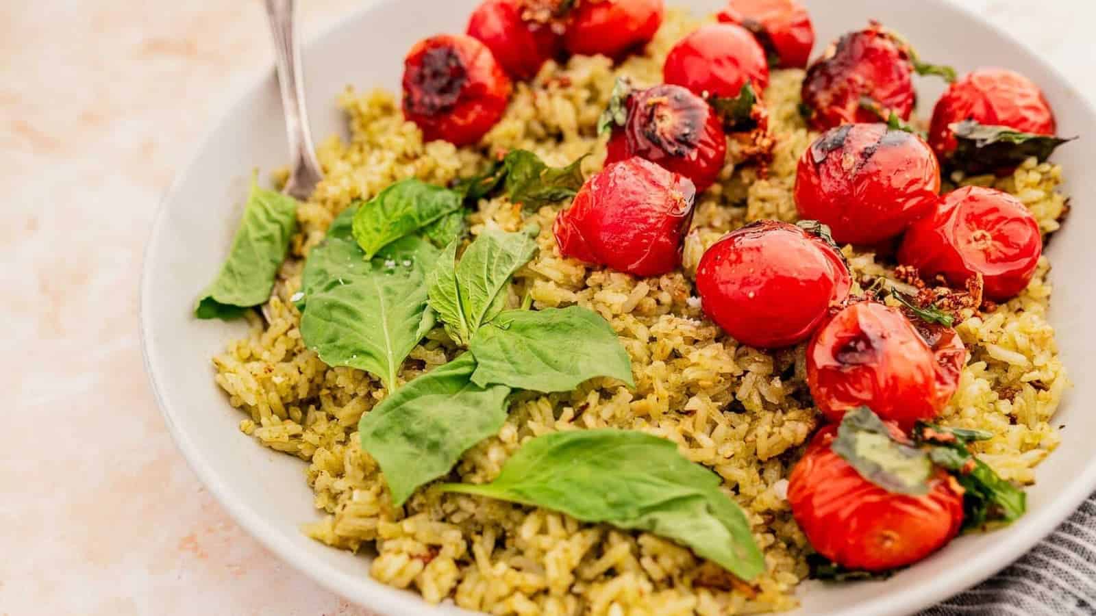 A plate of green rice topped with roasted cherry tomatoes and fresh basil leaves.
