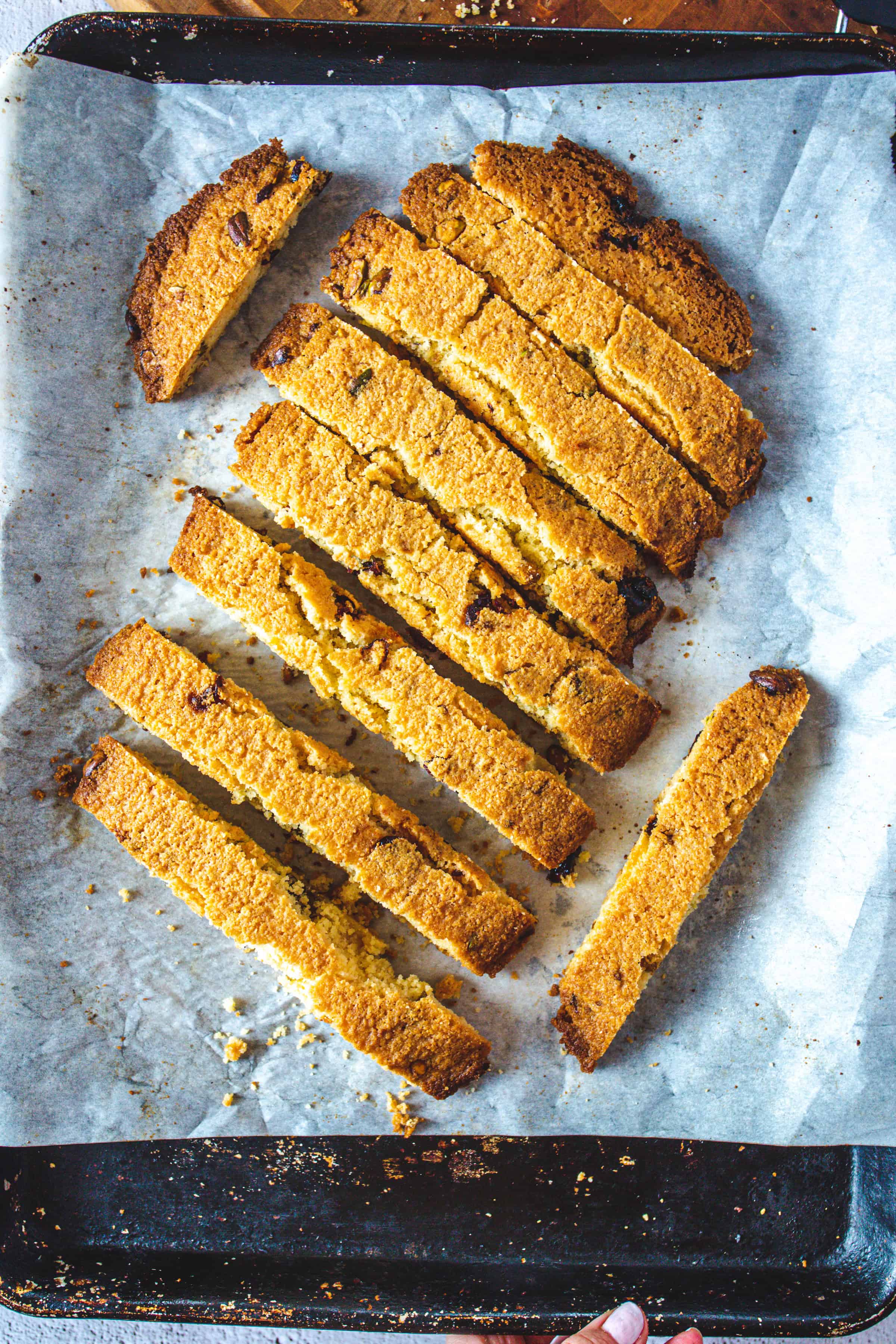 Sliced Pistachio Gluten-Free Biscotti with chocolate chips on a parchment-lined baking sheet.