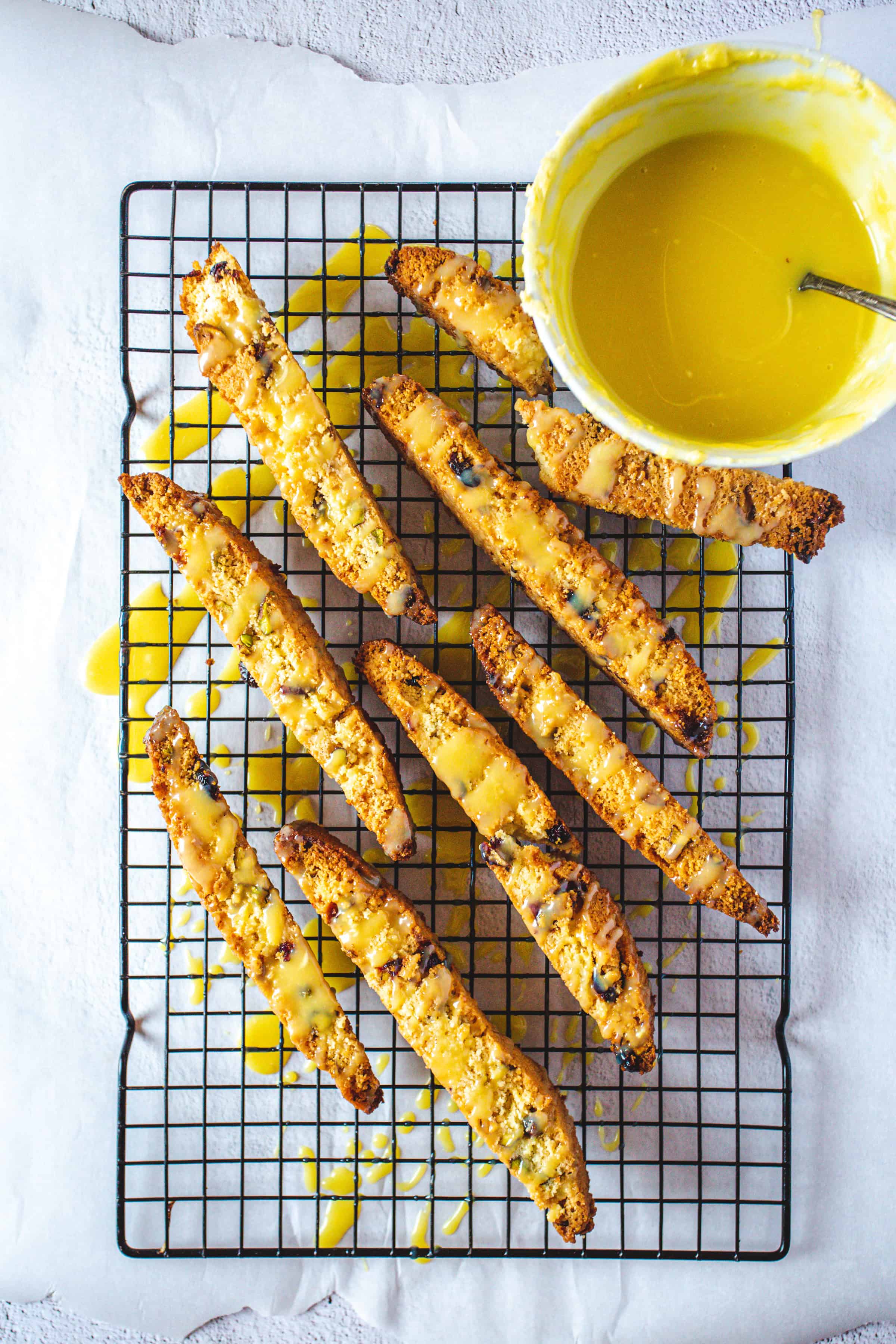 Breaded zucchini fries on a cooling rack, drizzled with a yellow sauce from a nearby bowl, create a savory scene reminiscent of Pistachio Gluten-Free Biscotti served fresh and delicious.