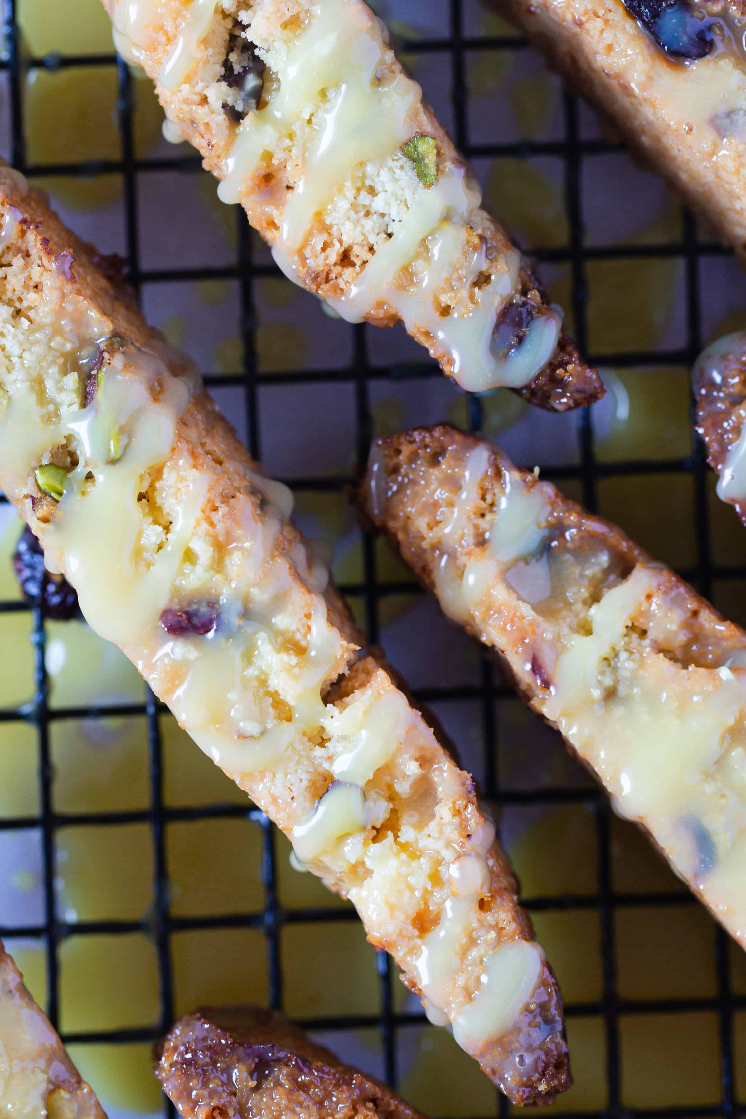 Pistachio Gluten-Free Biscotti drizzled with white icing, cooling on a black wire rack.
