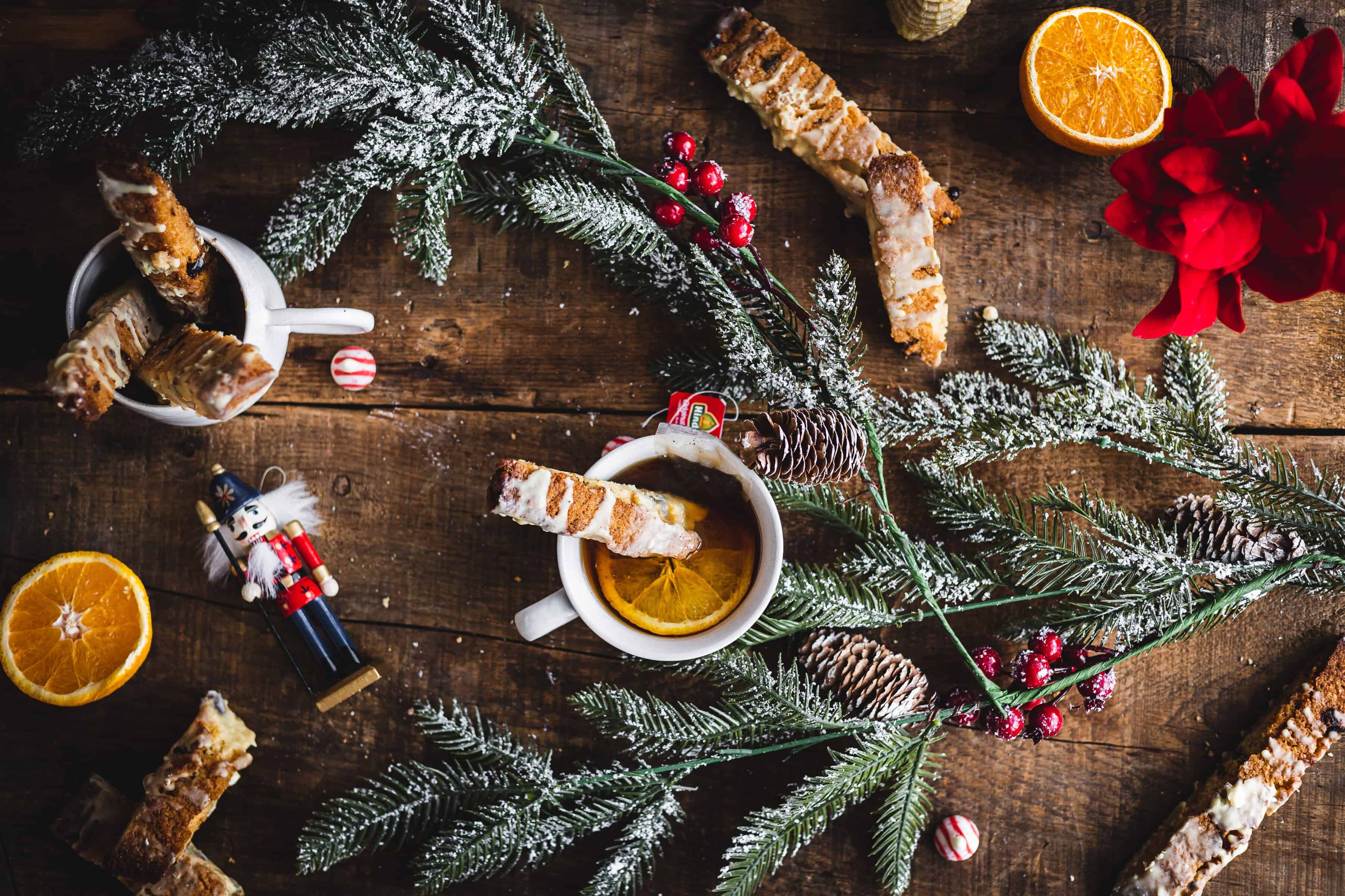Festive winter scene with Pistachio Gluten-Free Biscotti, oranges, pine branches, a nutcracker, and holiday decorations arranged on a wooden table.
