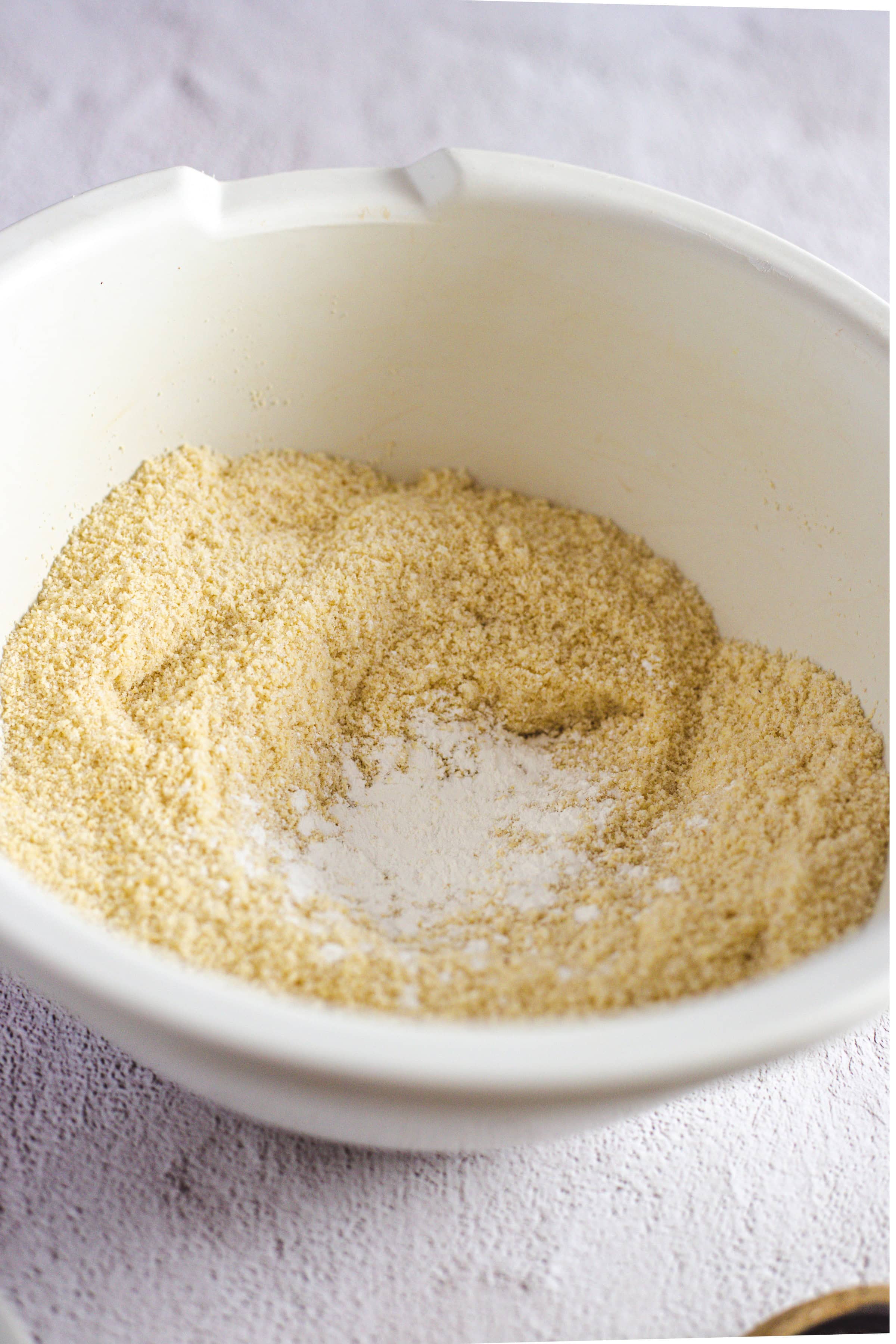 A white bowl filled with a mixture of flour and baking powder, ready for creating delicious Pistachio Gluten-Free Biscotti, sits on a light surface.