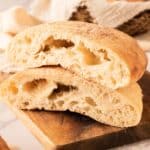 Two halves of ciabatta bread with airy, open crumb on a wooden board.
