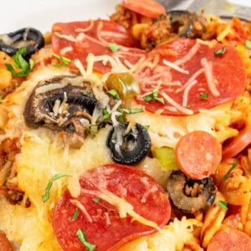 A plate of pasta topped with melted cheese, pepperoni, mushrooms, olives, and tomato sauce.