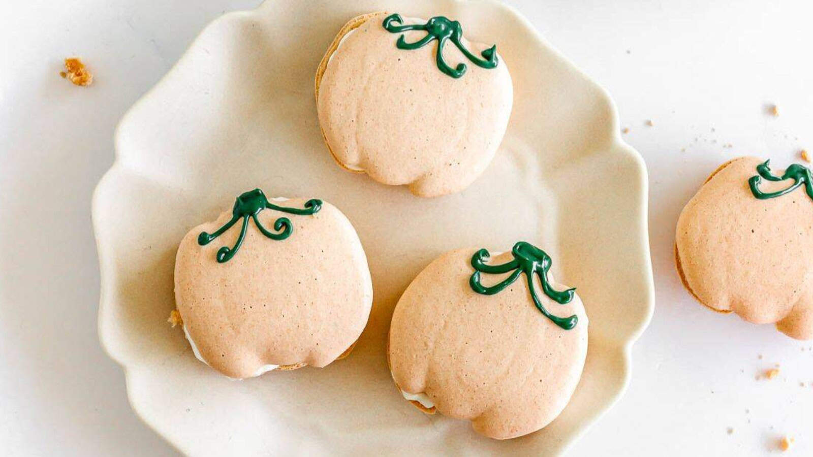 Pumpkin-shaped macarons with green icing stems on a white plate.