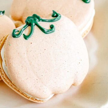 Pumpkin-shaped macarons with green icing stems on a white plate.