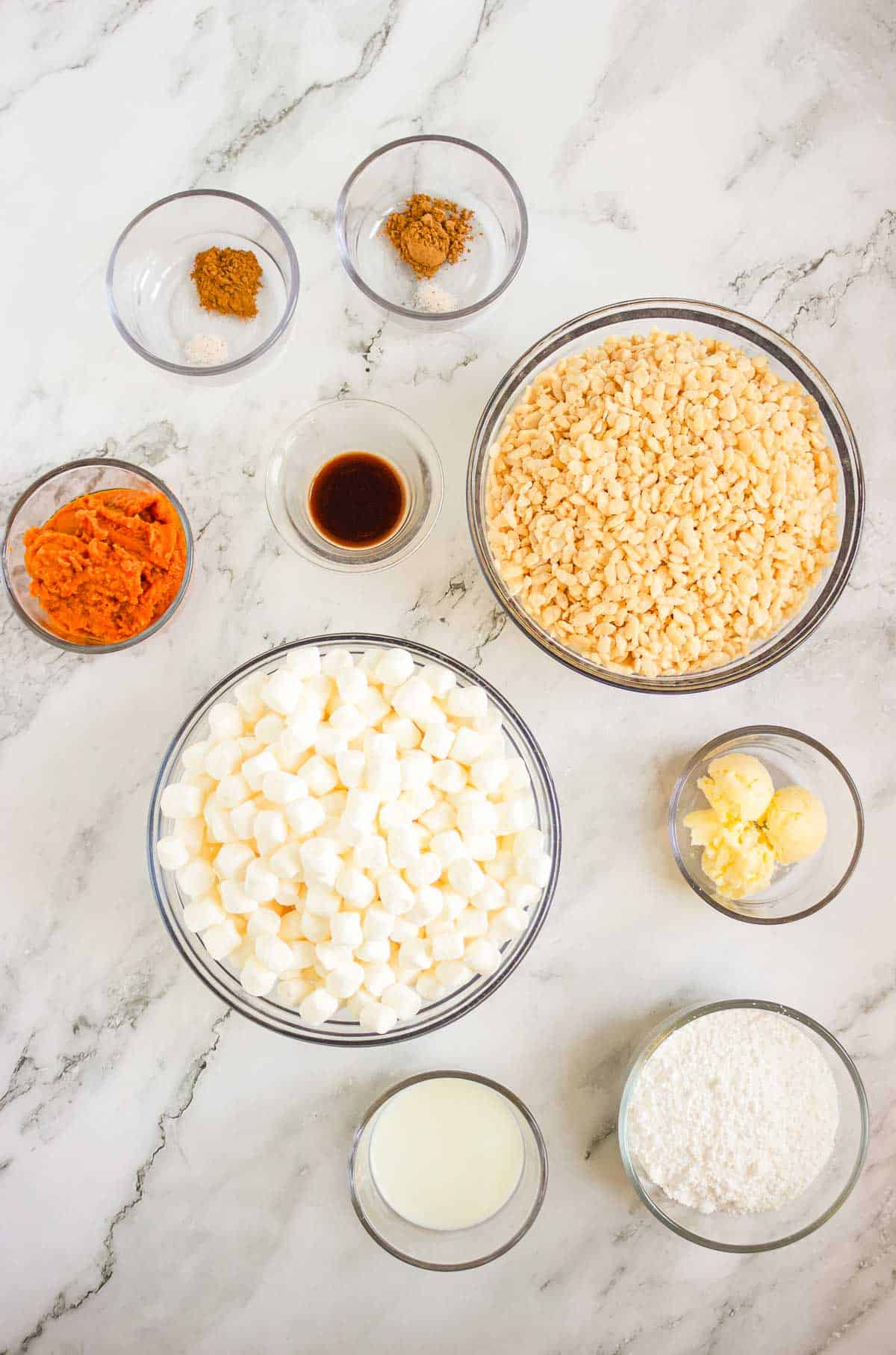 Ingredients for Pumpkin Rice Krispies Donuts: rice cereal, marshmallows, butter, pumpkin, spices, vanilla, coconut, and milk in bowls.