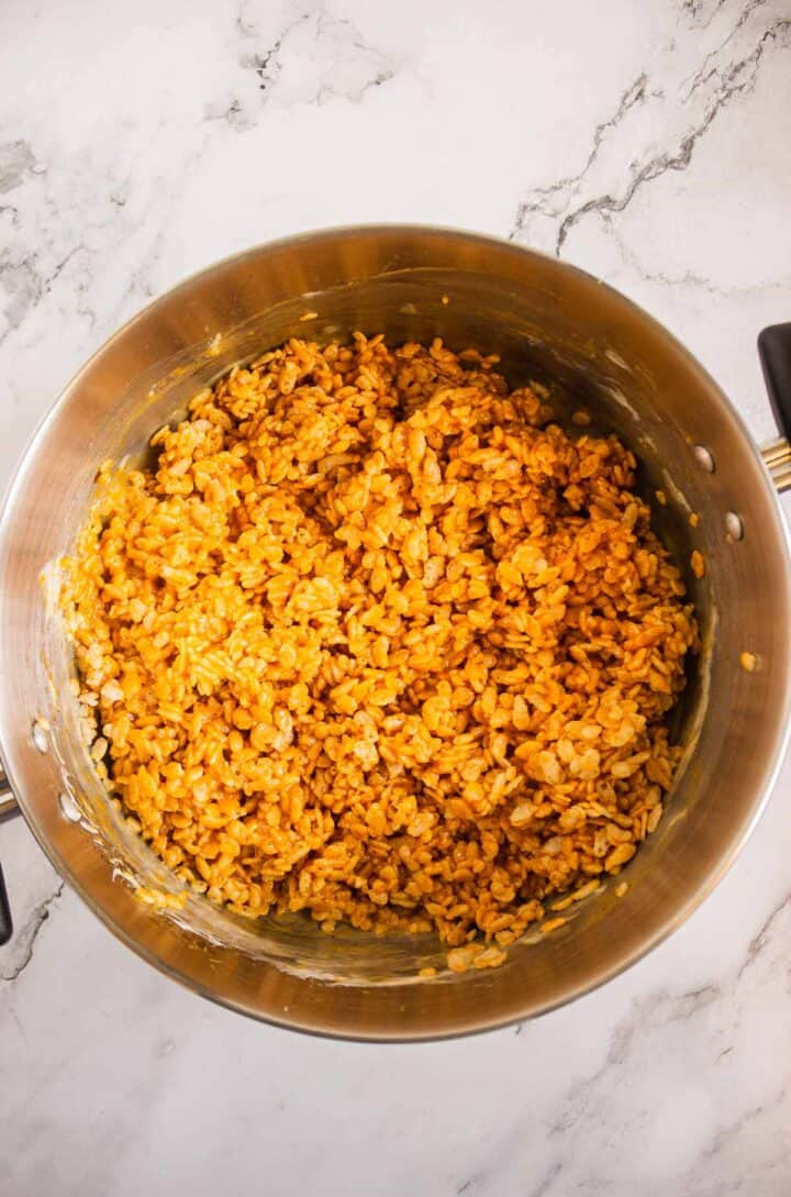 A pot of orange-colored, pumpkin-inspired seasoned rice sits on a marble countertop, reminiscent of Pumpkin Rice Krispies Donuts.