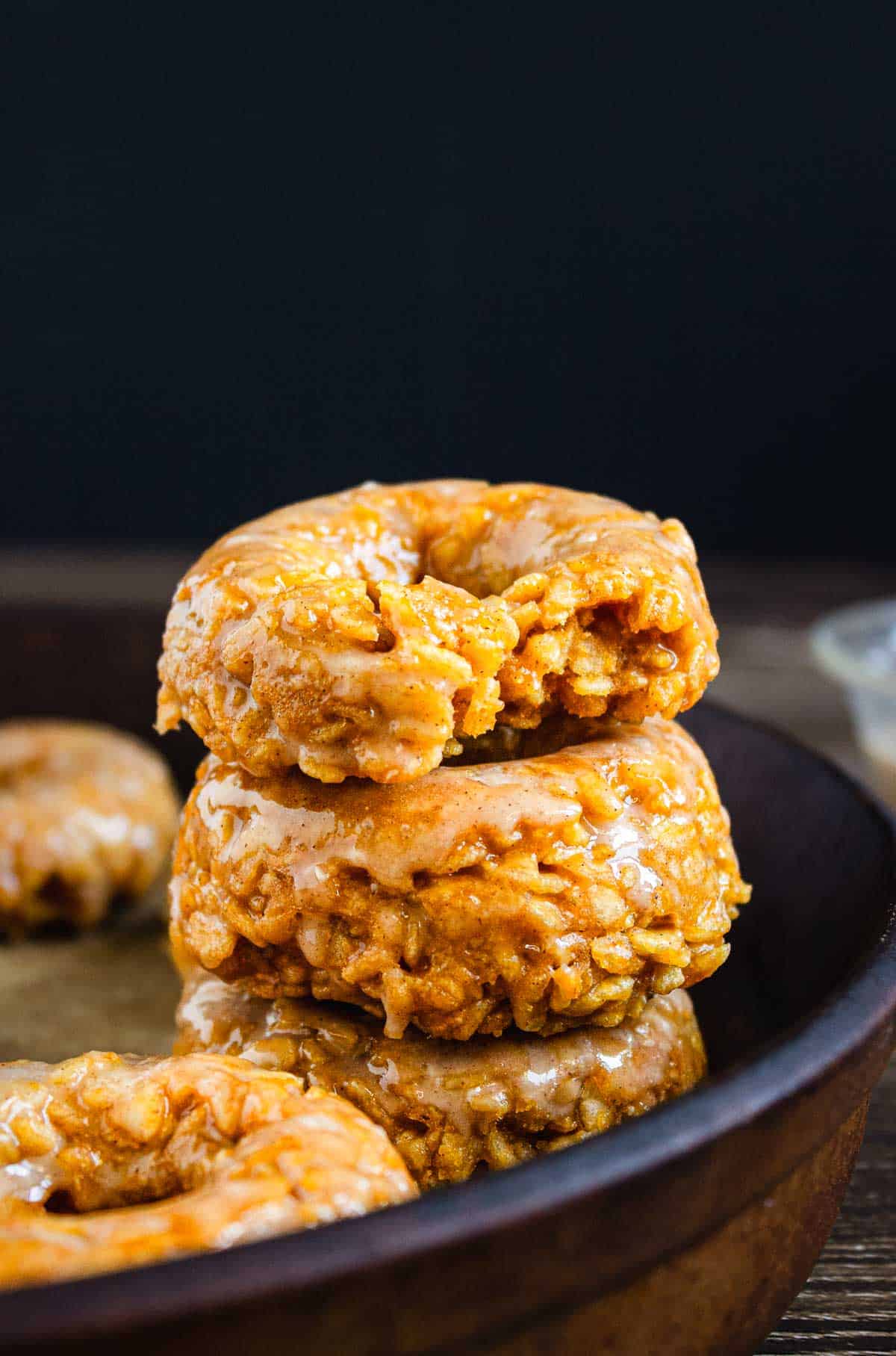 Three Pumpkin Rice Krispies Donuts are stacked on a plate, with the top donut showing a bite taken out of it.