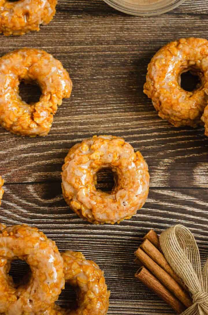 Glazed apple fritters and Pumpkin Rice Krispies on a rustic wooden table with cinnamon sticks in the corner.