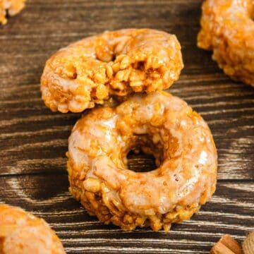 Two Pumpkin Rice Krispies Donuts, one stacked and one partially bitten, rest on a rustic wooden surface.