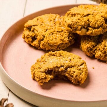 A plate of pumpkin cookies, one with a bite taken out, on a light pink dish.